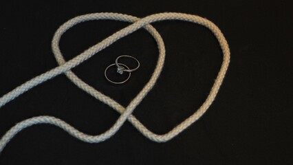 Tying the knot: heart shaped rope, one plain silvery ring and one diamond ring, with a black...