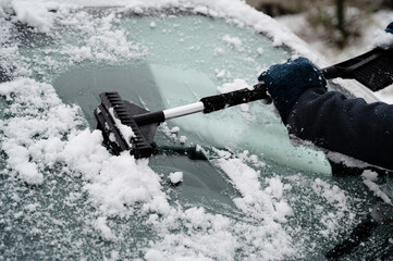 Driver is removing snow from car windshield with ice scraper and broom, clean car window from icy...