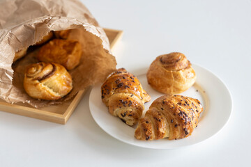 Fresh pastries - croissants with chocolate chips, poppy seed buns on a white sheet of paper on the table. Place for text