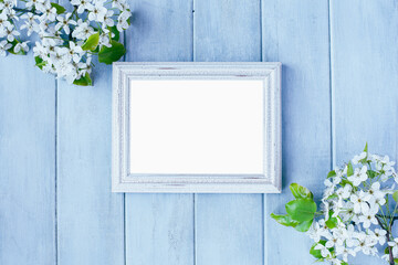 Blank empty rustic white picture frame over blue background with spring flowers. Table top view.