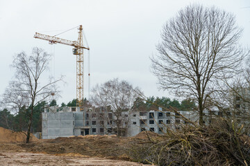 Silhouettes of working construction cranes against the background of an unfinished residential building. Multi-storey luxury apartment building on a construction site
