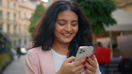 Happy laughing smiling portrait Indian Arabian ethnic woman girl female student businesswoman walking city street looking reading hold mobile cell phone telephone toothy smile online chatting outside - Powered by Adobe