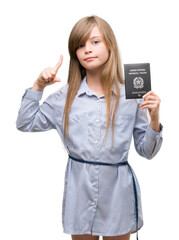 Young blonde toddler holding italian passport surprised with an idea or question pointing finger with happy face, number one