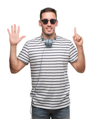 Naklejka premium Handsome young man wearing headphones showing and pointing up with fingers number six while smiling confident and happy.