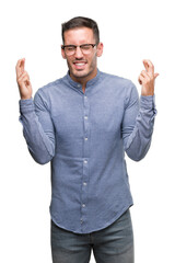 Fototapeta premium Handsome young elegant man wearing glasses smiling crossing fingers with hope and eyes closed. Luck and superstitious concept.