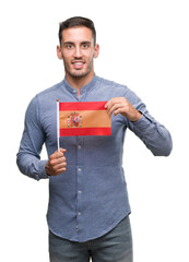 Handsome young man holding a flag of Spain with a happy face standing and smiling with a confident smile showing teeth