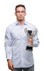 Handsome young man holding trophy with a confident expression on smart face thinking serious