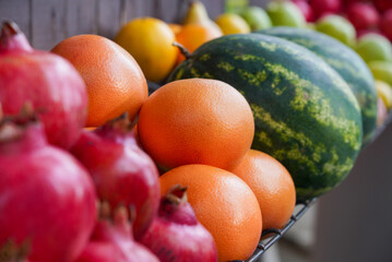 Exotic fruits arranged on a fresh stand. Focus on grapefruit. In the background watermelon, oranges, apples. In the foreground is a pomegranate.