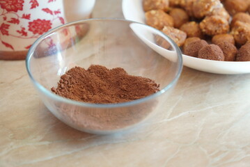 Natural cocoa in a glass bowl. In the background, biscuit candies that will be covered with cocoa.