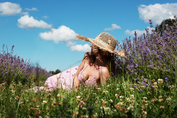 Young beautiful woman in a straw hat is lying resting in a lavender field against the background of the sky.	