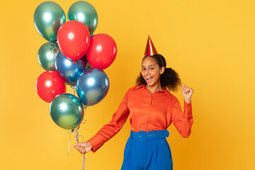 Fototapeta na wymiar African girl posing with festive balloons and birthday hat, studio