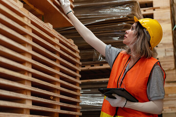 Fototapeta premium woman worker carpenter wearing safety uniform and hard hat working and checking the quality of wooden products at workshop manufacturing. man and woman workers wood in dark warehouse industry.