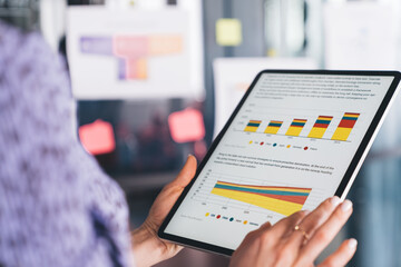 Selective focus on modern touch pad with browsed financial web page, unrecognizable female corporate director using digital tablet for analyzing business marketing and graph charts while working