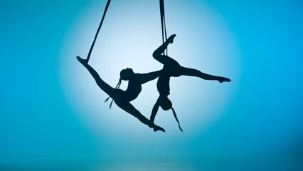 Silhouette of two female acrobats isolated on blue neon background. Girls aerial dancers performing...