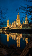 Basilica's Twilight Dance: Moonlit Zaragoza showcases the Pilar, Stone Bridge, and Ebro River in an exquisite nocturnal ballet.

