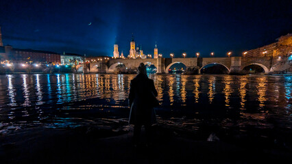 River of Reflections: A woman's backlit beauty harmonizes with Zaragoza's night, a vision by the...