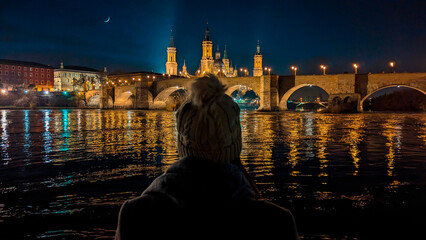 Zaragoza Illumination: Backlit beauty gazes at Pilar, Ebro, Stone Bridge—serenity in the night.

