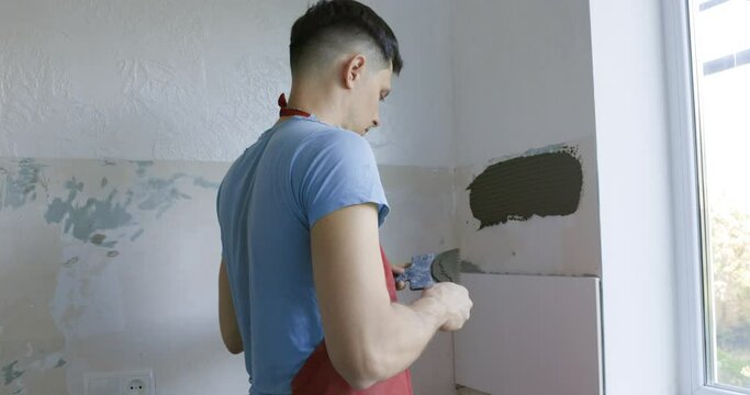 male master glues ceramic tiles on the wall. Laying white tiles in the kitchen
