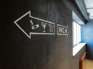 Arrow direction to smoking area, toilet icon, WC symbol on black wall, nightclub, public toilet.