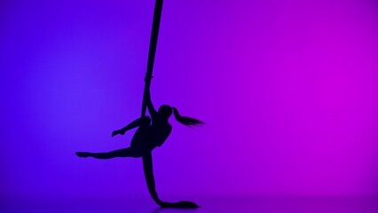 Silhouette of female acrobat isolated on colorful neon background. Girl aerial dancer performing acrobatic element on air silk.