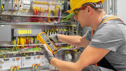 The electrician works with multimeter during connects the wiring in the fuse box. Work in electrical industry.