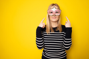 Portrait of attractive beautiful young woman wearing carnival mask isolated yellow background.