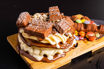 Pancake artigianali con crema di cioccolato bianco e cioccolato al latte, praline di cioccolato e barrette di cioccolato sopra come decorazione accompagnato da altre barrette e cioccolato