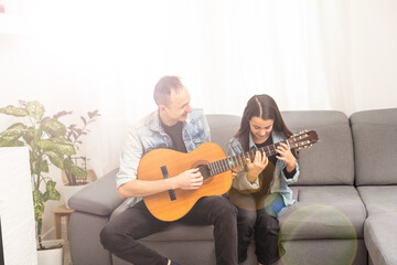 Father guy teaching girl teenager daughter guitar playing at home. Family musical lessons with strings instrument