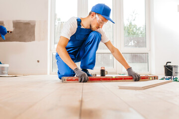 Close up hands of repairman in grey gloves and special uniform laying tiles with tile leveling system on the floor in a new house	
