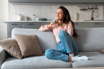 Content woman savoring coffee on comfortable couch