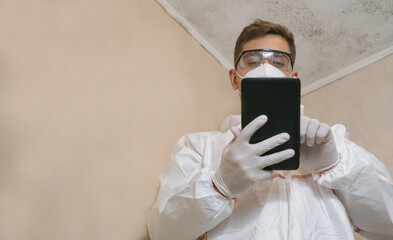 a man looking at a musty white wall. Makes notes about cleaning on your phone. Specialist of...