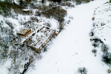 aerial view of an abandoned old collapsed building by a frozen river on a winter day