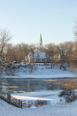  Winter city landscapes of Kuldiga, Latvia. Ancient buildings through a pattern of trees. Vertical frame. he Evangelical Lutheran Church of Saint Catherine. View from across the Venta Rive