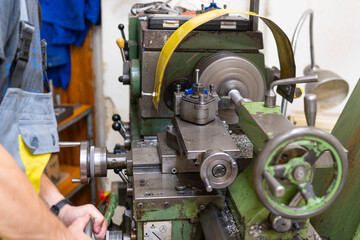 A worker working on an old green lathe machine in a workshop