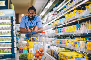 Black Male Buyer Shopping Groceries In Supermarket Taking Product From Shelf Standing With Shop...
