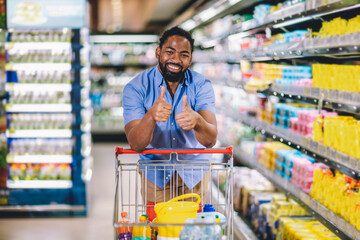 Black Male Buyer Shopping Groceries In Supermarket Taking Product From Shelf Standing With Shop...