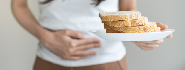 Gluten allergy, asian young woman hand holding, refusing to eat white bread slice on plate in breakfast food meal at home, girl having a stomach ache. Gluten intolerant and Gluten free diet concept.