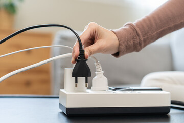 Closed up hand of woman plugged in, unplugged electricity cord cable on socket on table for energy saving, electric power on plate outlet, control expense electrical appliances, environment concept.