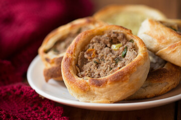 Esfihas Meat puff pastry on a white plate with a red cloth and a wooden table
