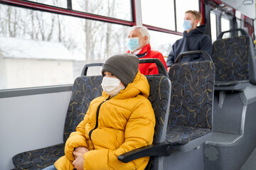 Side view of little boy in protective mask and grey cap folding hands and passengers behind sitting...