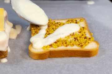 Preparing process of Croque monsieur and croque madame, grilled sandwiches with sliced ham, melted cheese, dijon mustard and poached egg on  bechamel sauce.