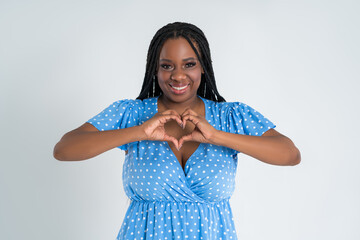 Happy plus size female model posing in blue dress on white background and showing heart sign, young...