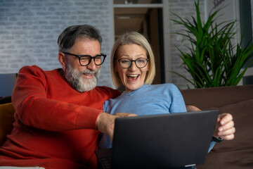 Husband and wife watching a funny movie or tv show on laptop. Happy couple using the laptop. Home...