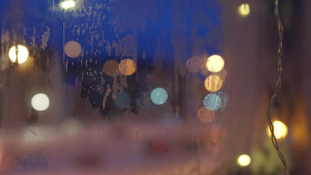 Defocused bokeh garland light reflected in frozen window glass at dusk in winter. Christmas and New Year holidays background.