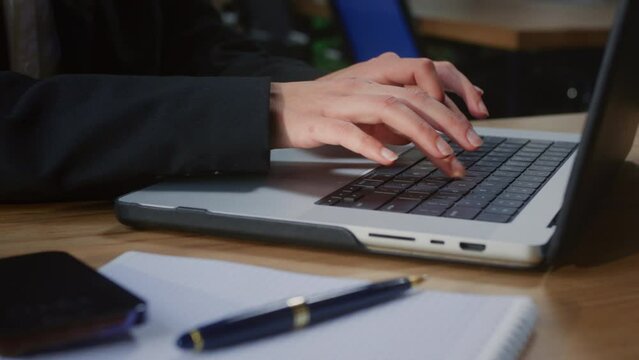 Businesswoman types proposals for potential clients customizing details on modern laptop. Professional office worker types messages to team members and reviews reports using device at table