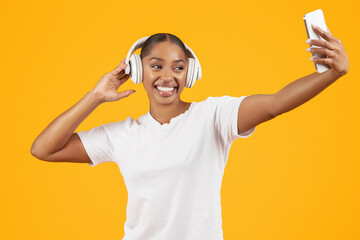 black lady making selfie listening music with earphones, yellow background