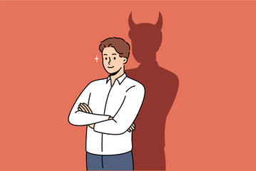 Confident businessman with bad thoughts stands with arms crossed near shadow with devil horns. Bad male office worker with treacherous ideas, wants to achieve goal in unethical way - obrazy, fototapety, plakaty