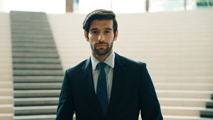Portrait of Serious business man looking at camera while standing at stairs. Closeup of successful man staring at camera while wearing business suit. Happy executive manager look at camera. Exultant. - obrazy, fototapety, plakaty