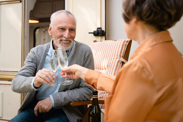Cheerful happy elderly senior old couple celebrating anniversary special event drinking wine champagne while traveling in camper van trailer together on holidays