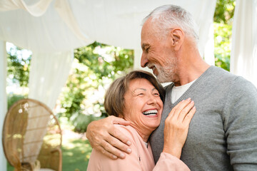 Active senior old elderly couple family spouses grandparents hugging embracing bonding, spending quality time together outdoors in the garden